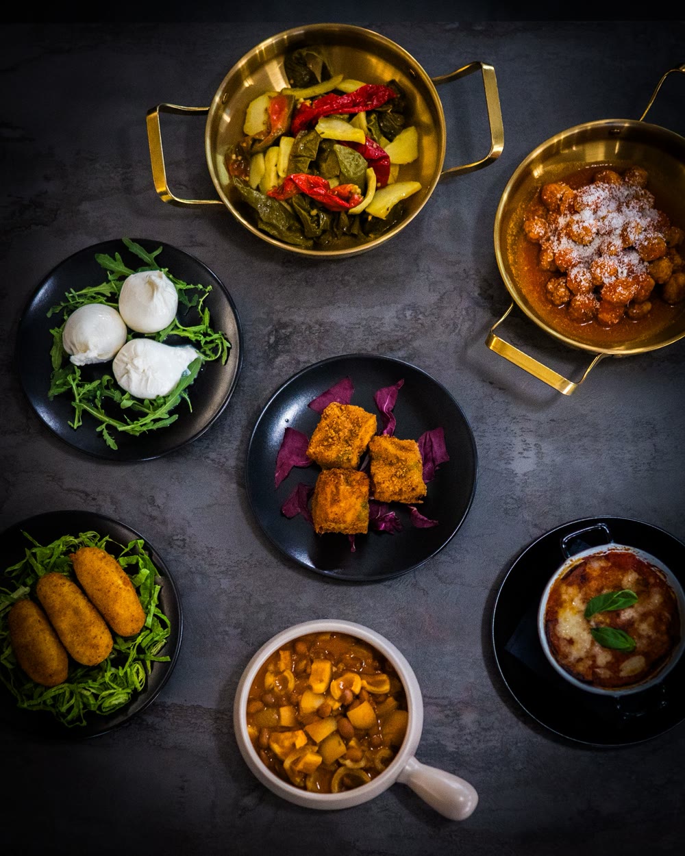 Antipasti visti dall'alto: burrata con rucola, crocchè, parmigiana e padelle dorate con le portate calde