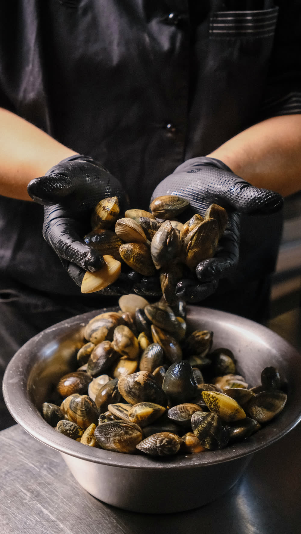 Mani con guanti neri versano le cozze in una ciotola d'acciaio